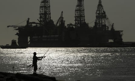 A man wears a face mark as he fishes near docked oil drilling platforms, Friday, May 8, 2020, in Port Aransas, Texas.