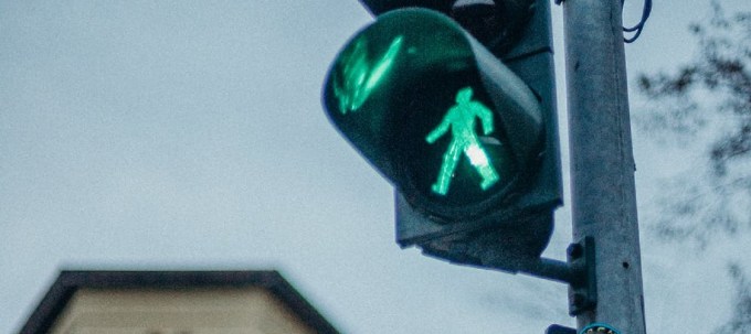 Crossing lamp with green illuminated person walking and a building in the background