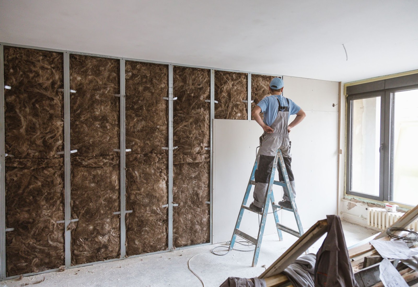 Home em cima de escada observa parede de drywall ainda em fase de construção. 