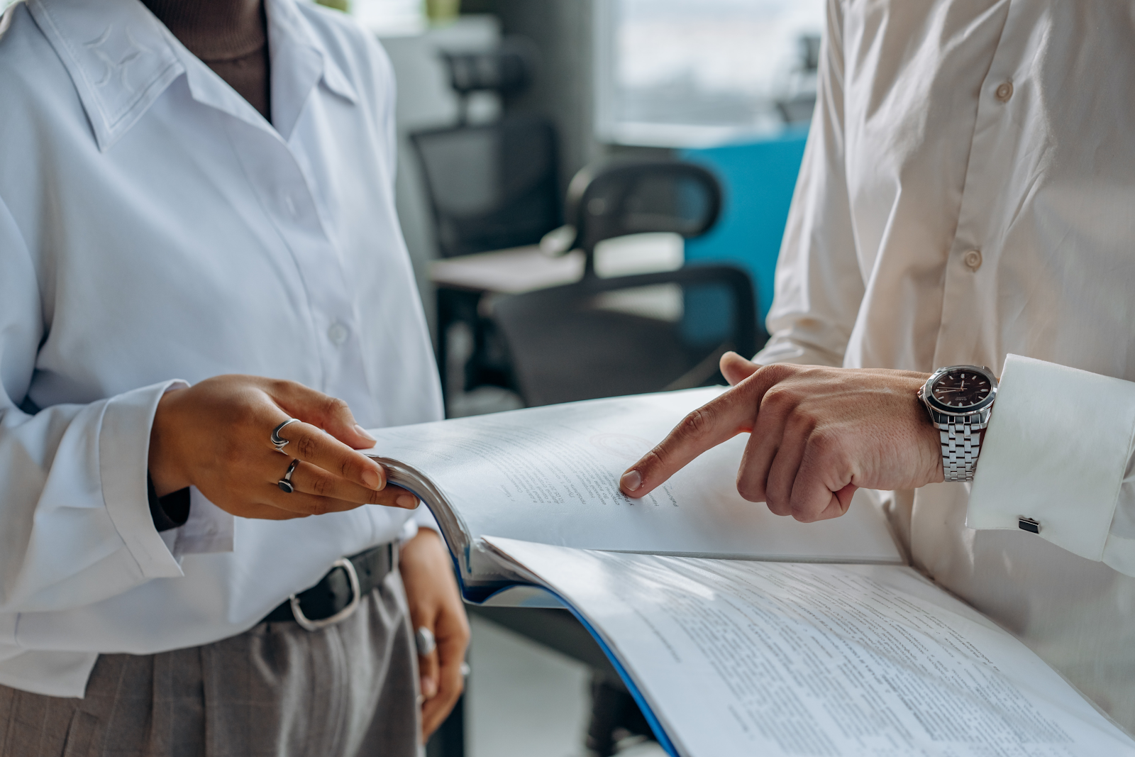 A person pointing to a line in the report another person is holding.