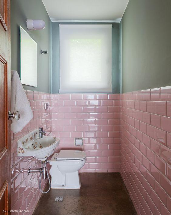 Banheiro com subway tiles rosa em meia parede com uma pintura na cor verde musgo  acima, pia branca simples e piso de cimento queimado antigo.