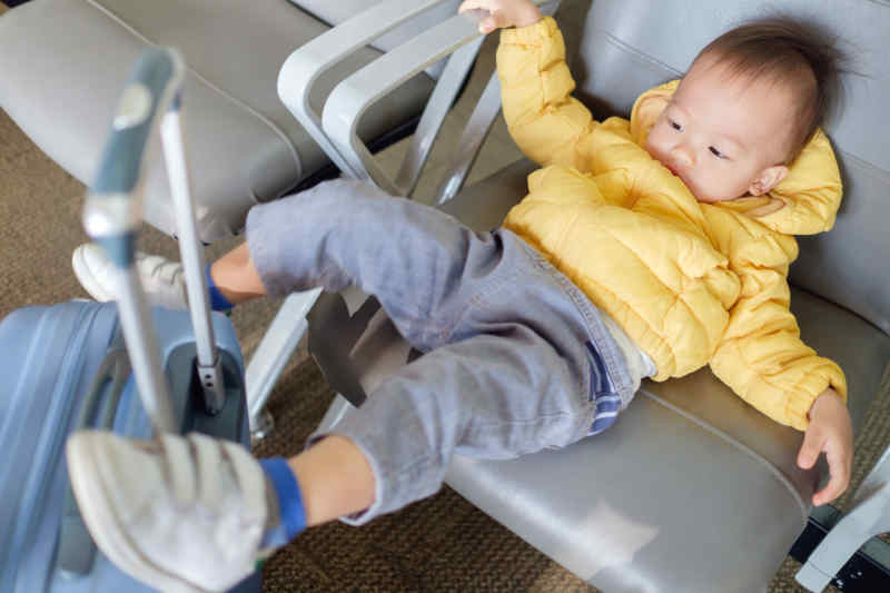 toddler sitting in airport terminal with suitcase