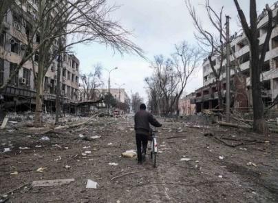 A man walks with a bicycle in a street damaged by shelling in Mariupol, Ukraine.