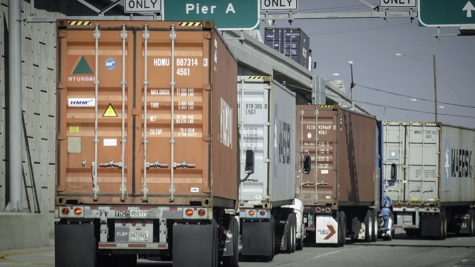 A rearview of four tractor-trailers waiting to enter the Port of Los Angeles
