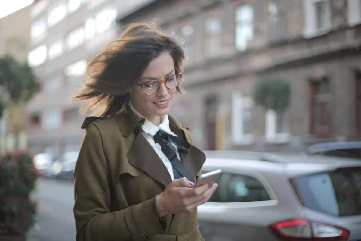 femeie citește mesaj telefon pe stradă zâmbind