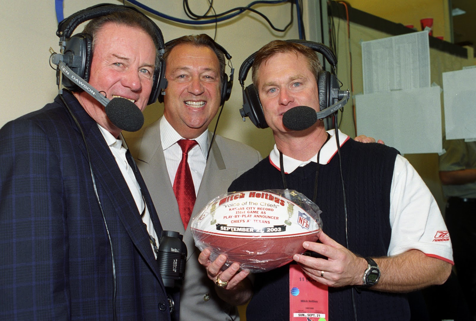 Holtus poses with Len Dawson and Carl Peterson, posing with a commemorative ball to celebrate Holtus's 151st game called.