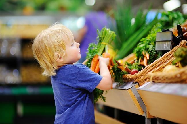 A little boy picking a bunch of fresh carrots off the vegetable stand in a grocery store.