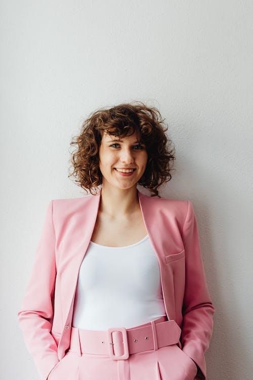 Free Woman in Pink Blazer Standing Against a White Wall Stock Photo