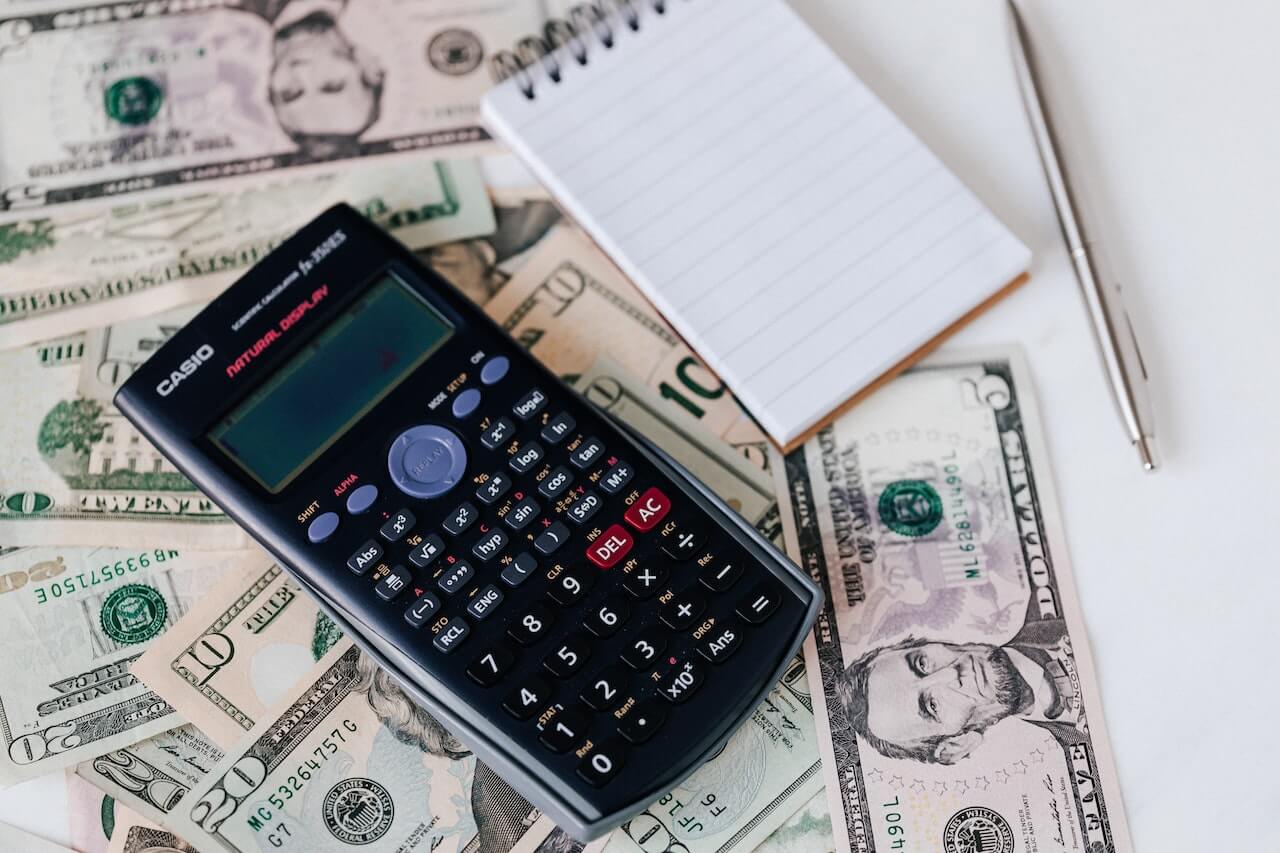 Various bills are scattered on a table with a calculator, notepad, and pen on top of or near them.