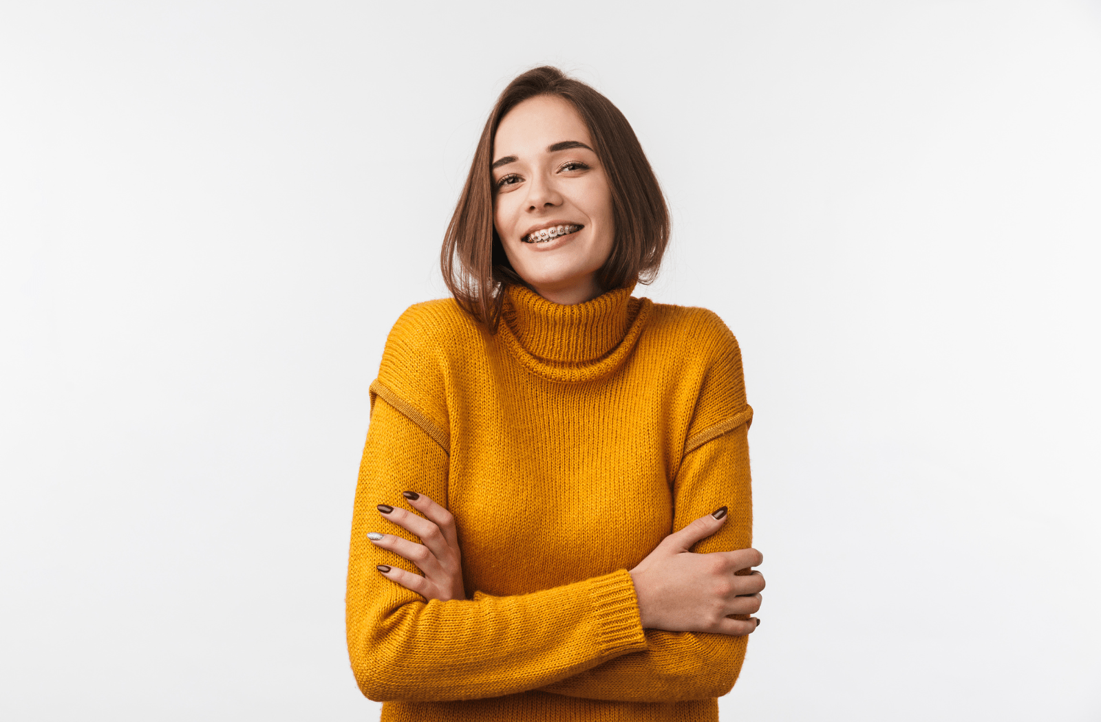 A young adult woman smiling with her braces showing, wearing a yellow sweater