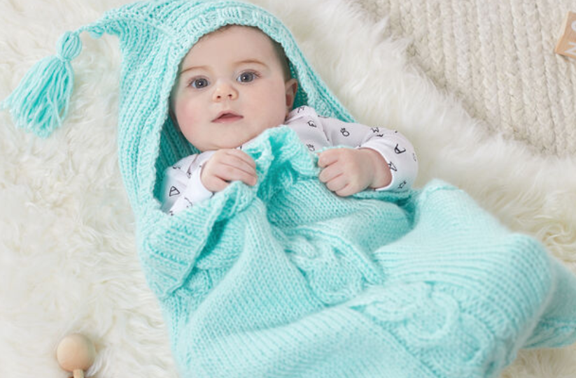 baby wearing a light blue bunting that has a hood and cable detail