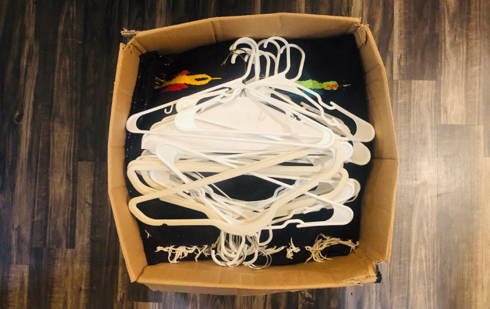Top view of an open moving box. It is packed with blankets and topped with nearly 20 hangers for added stability.