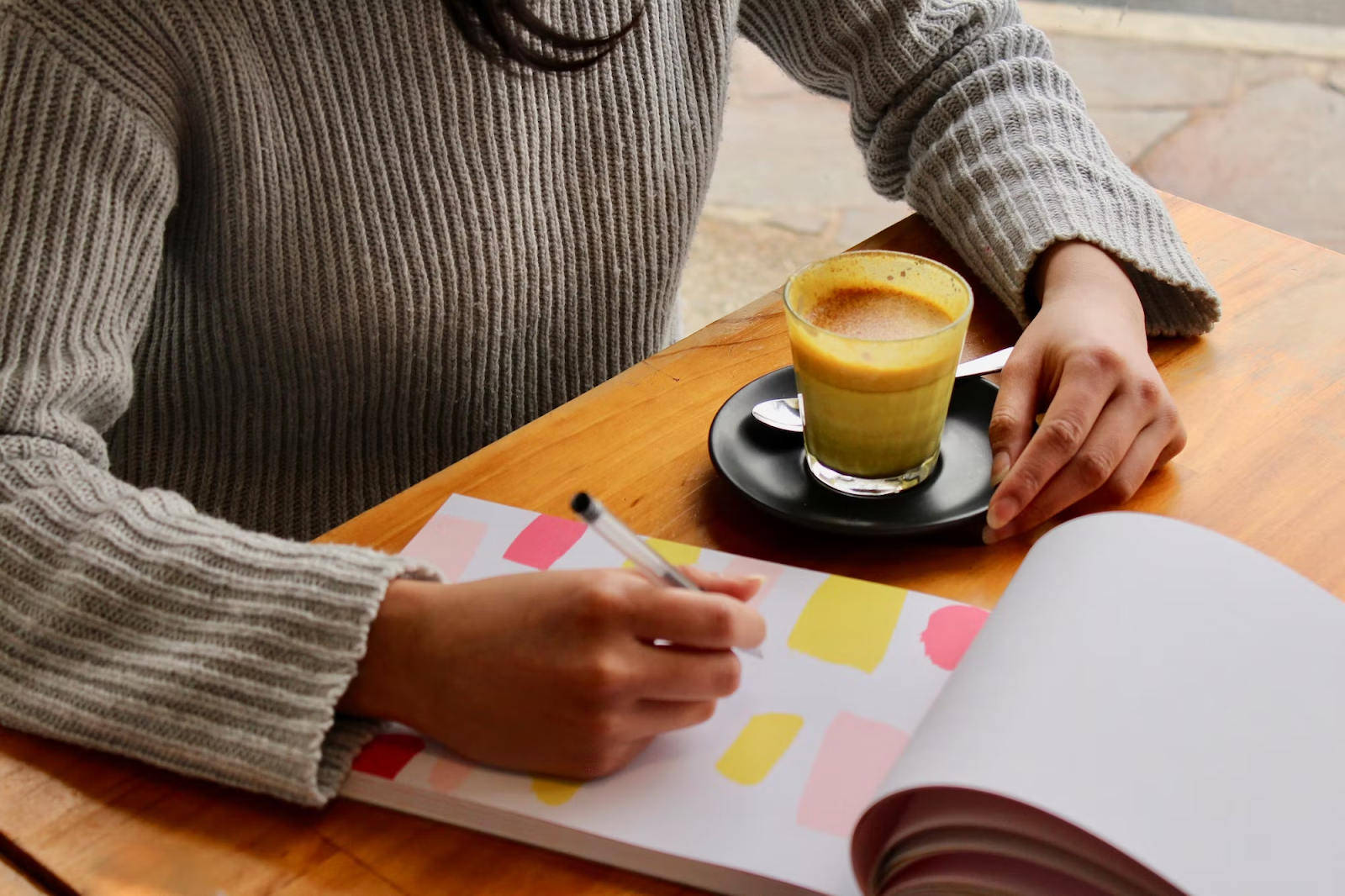 A person holding a pen above a notepad with a coffee mug beside them.
