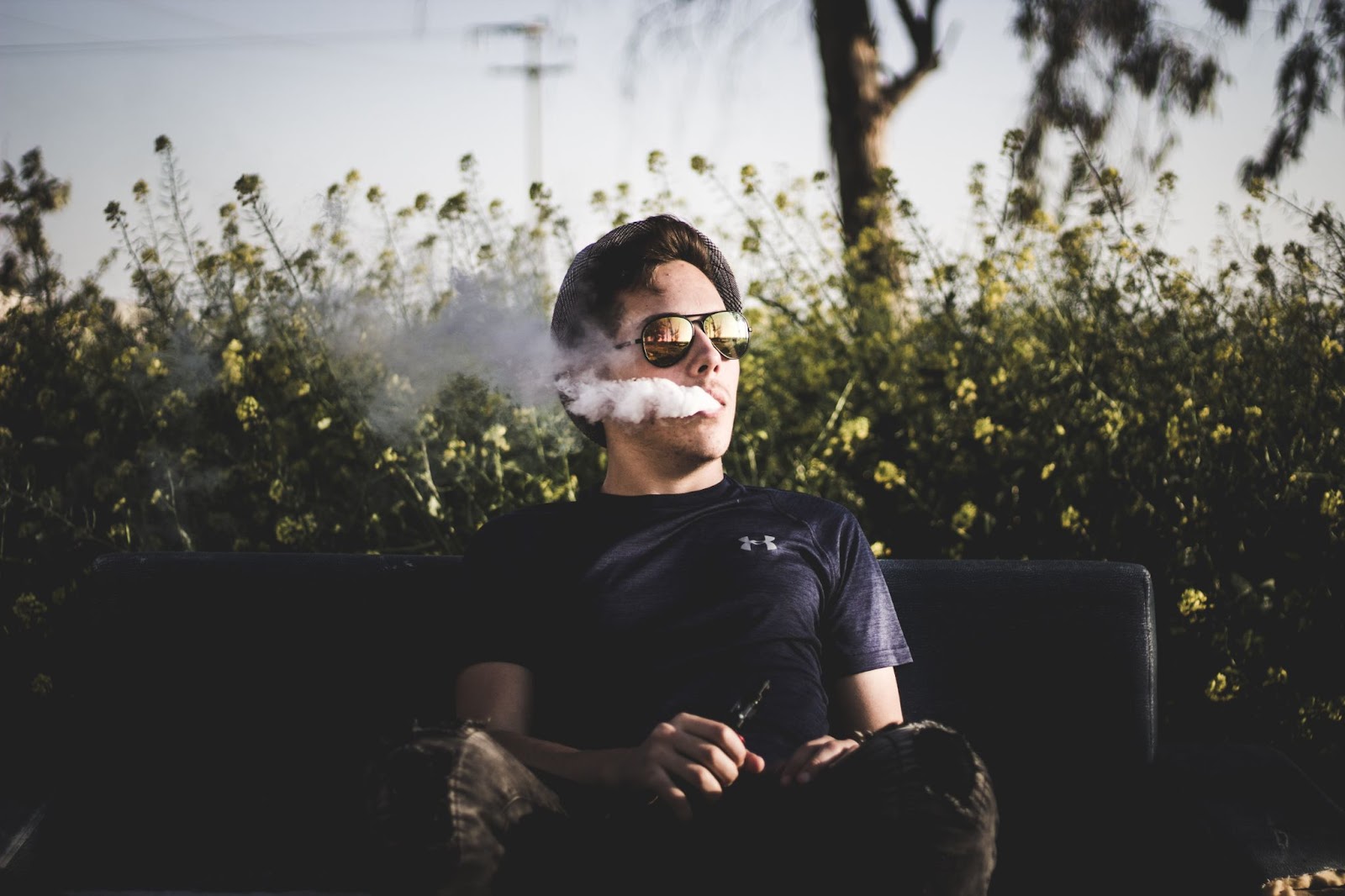 A boy sitting on the bench and and enjoying vaping