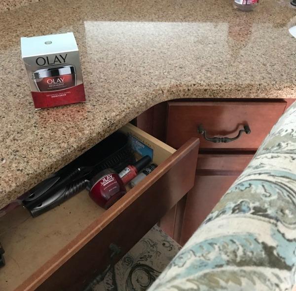  A jar of Olay Regenerist Cream on a counter with an open drawer with make up in it.
