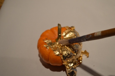 use paintbrush to tuck gold leaf into creases of pumpkin
