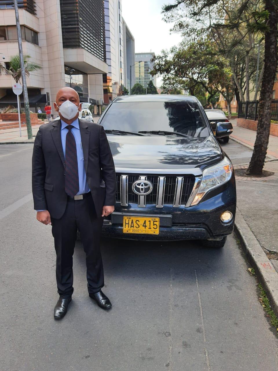 A person in a suit standing in front of a car

Description automatically generated