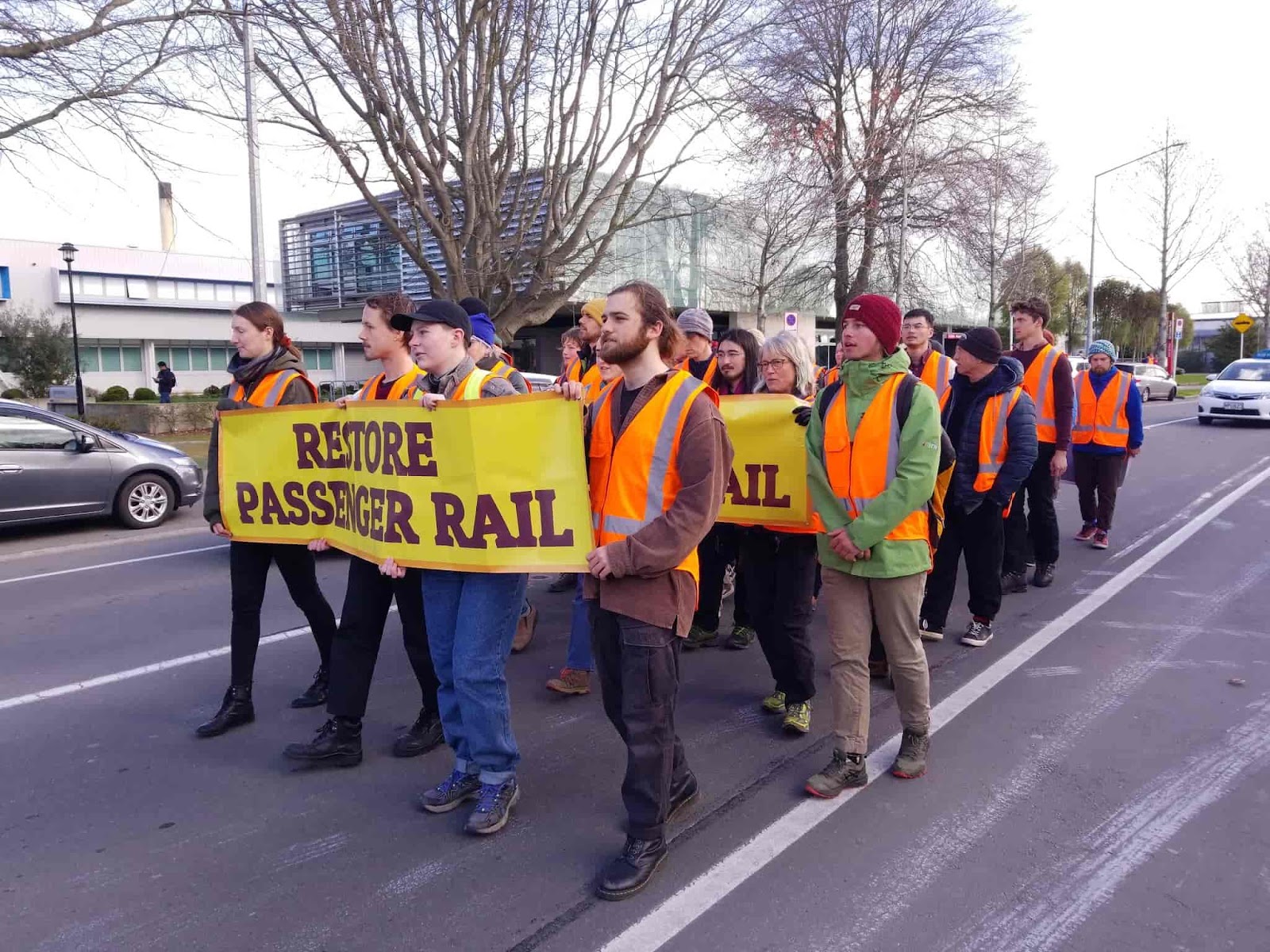 Activists slow march down the street holding Restore Passenger Rail banners