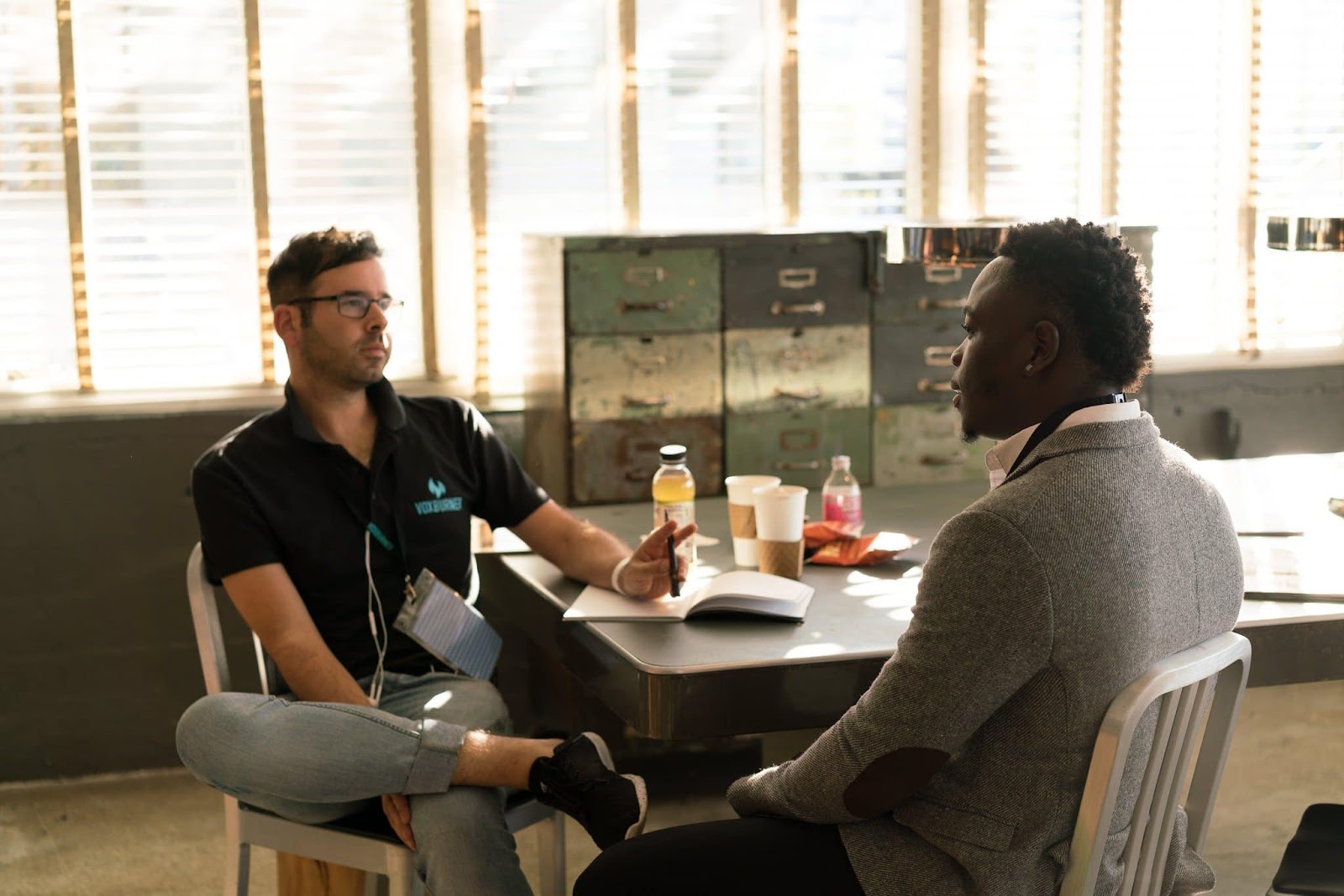 Two young men sitting at a table with a book, food, and coffee between the two of them