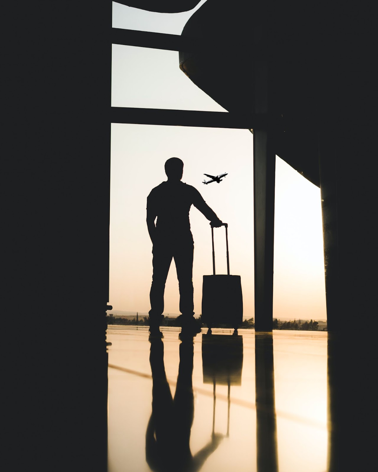 Man standing at airport with luggage watching plane take off