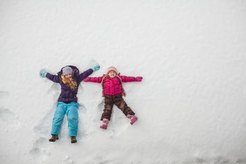 Two children making snow angels in snow