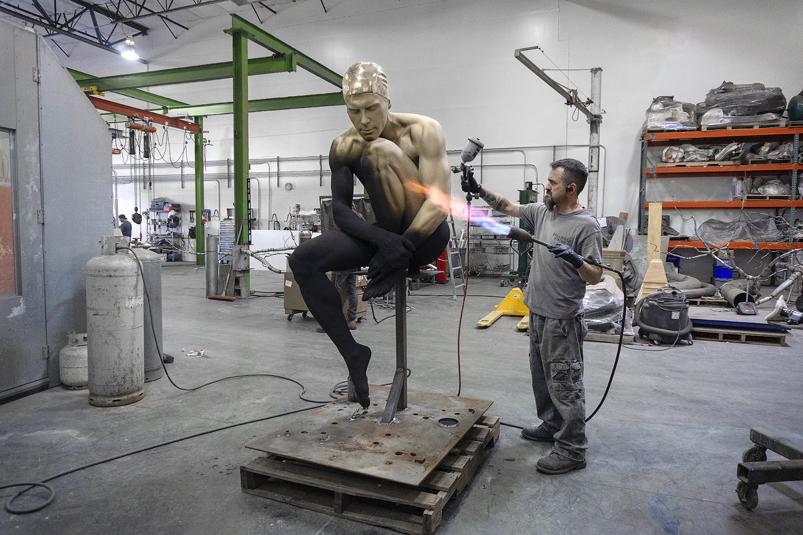 Bronze sculpture of diver seated with patina being applied to surface by artisan
