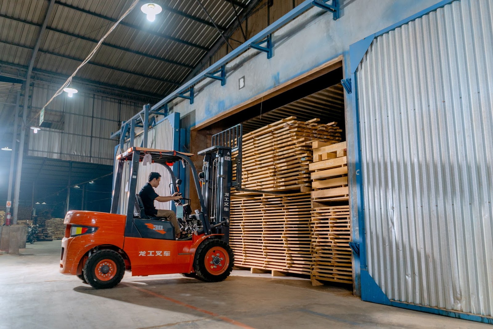 A person moving pallets inside of a warehouse using a red forklift