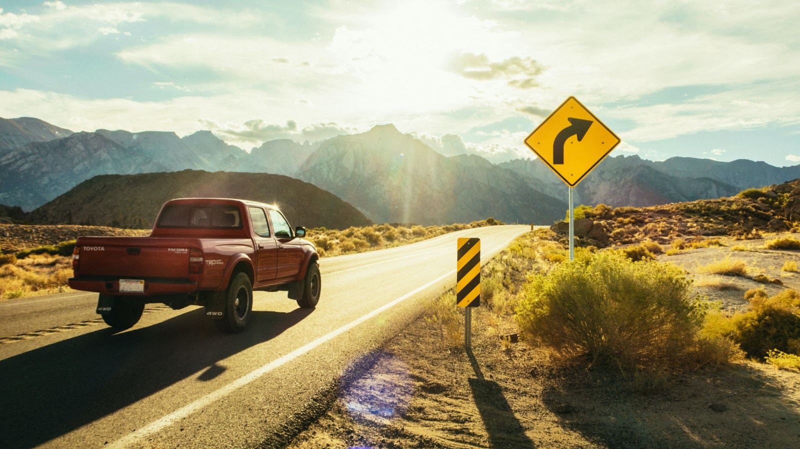 A Toyota Tacoma driving on a sunny mountain road with a yellow caution sign on the side of the road