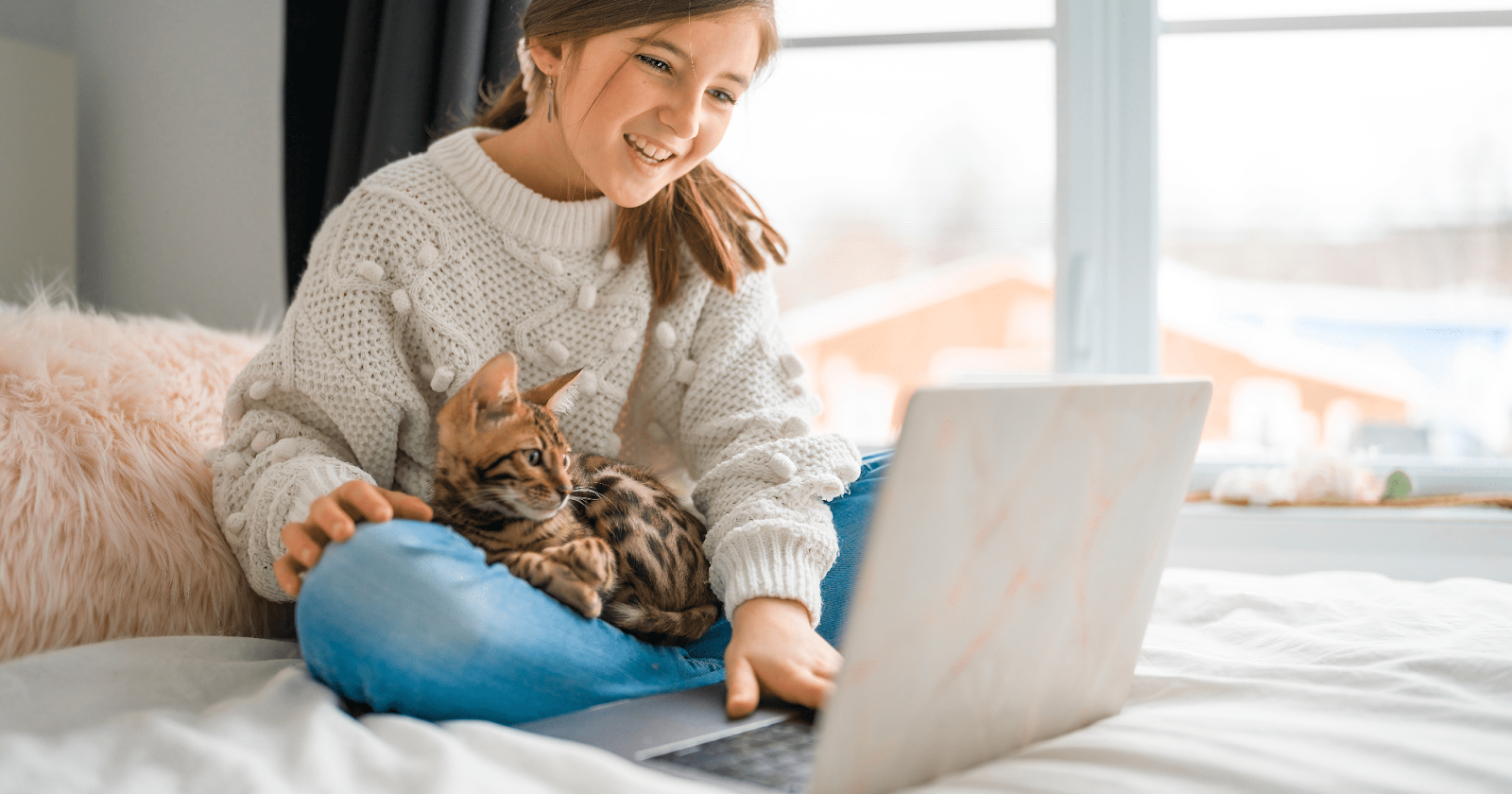 Girl working on laptop with Savannah cat in lap