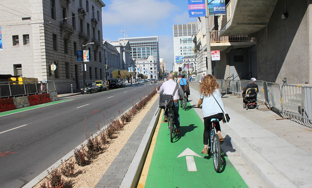 Image of cyclists commuting along an urban street using a protected bike lane with bright green paint.