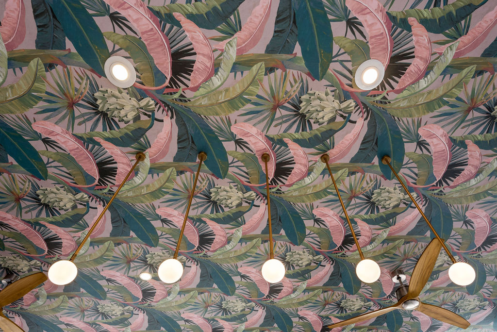 Ceiling design with vibrant tropical leaf wallpaper and modern gold light fixtures with round bulbs.