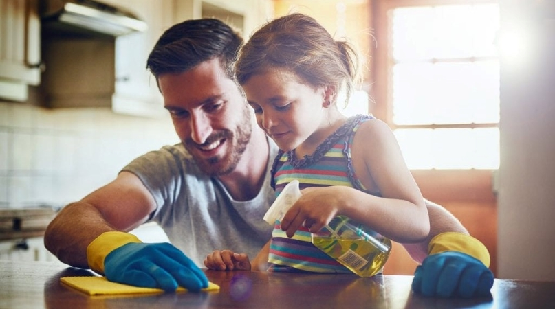 A father helping his young child clean.