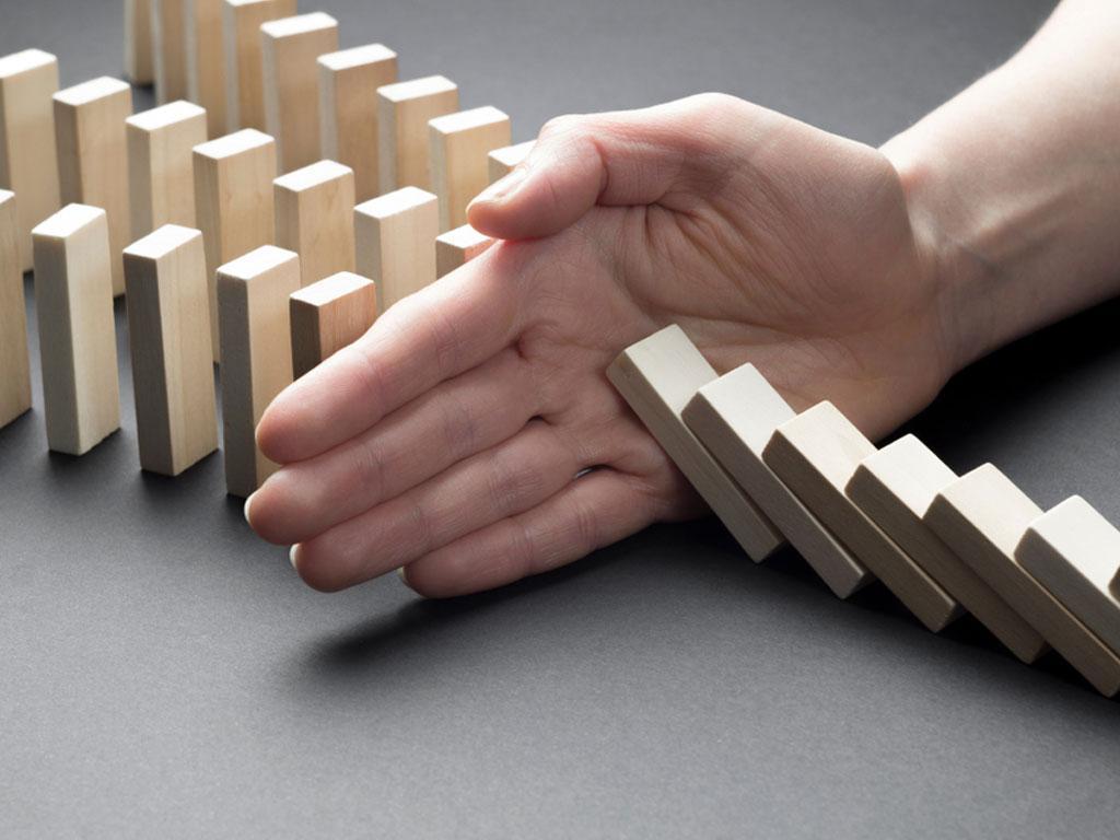 Uma mão impedindo uma fileira de dominós de cair.