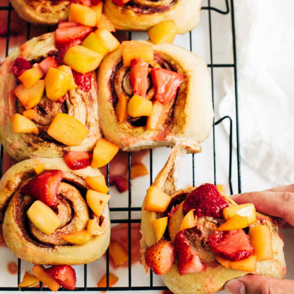 cinnamon rolls on a cooling rack topped with a strawberry and apple glaze