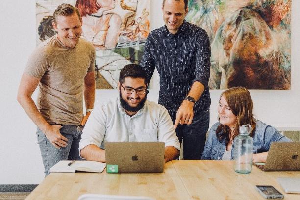 A group of people standing around a table with a computer

Description automatically generated with medium confidence