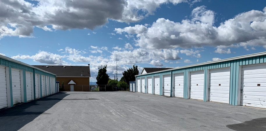 View of a self-storage center with over a dozen storage units under a cloudy blue sky.