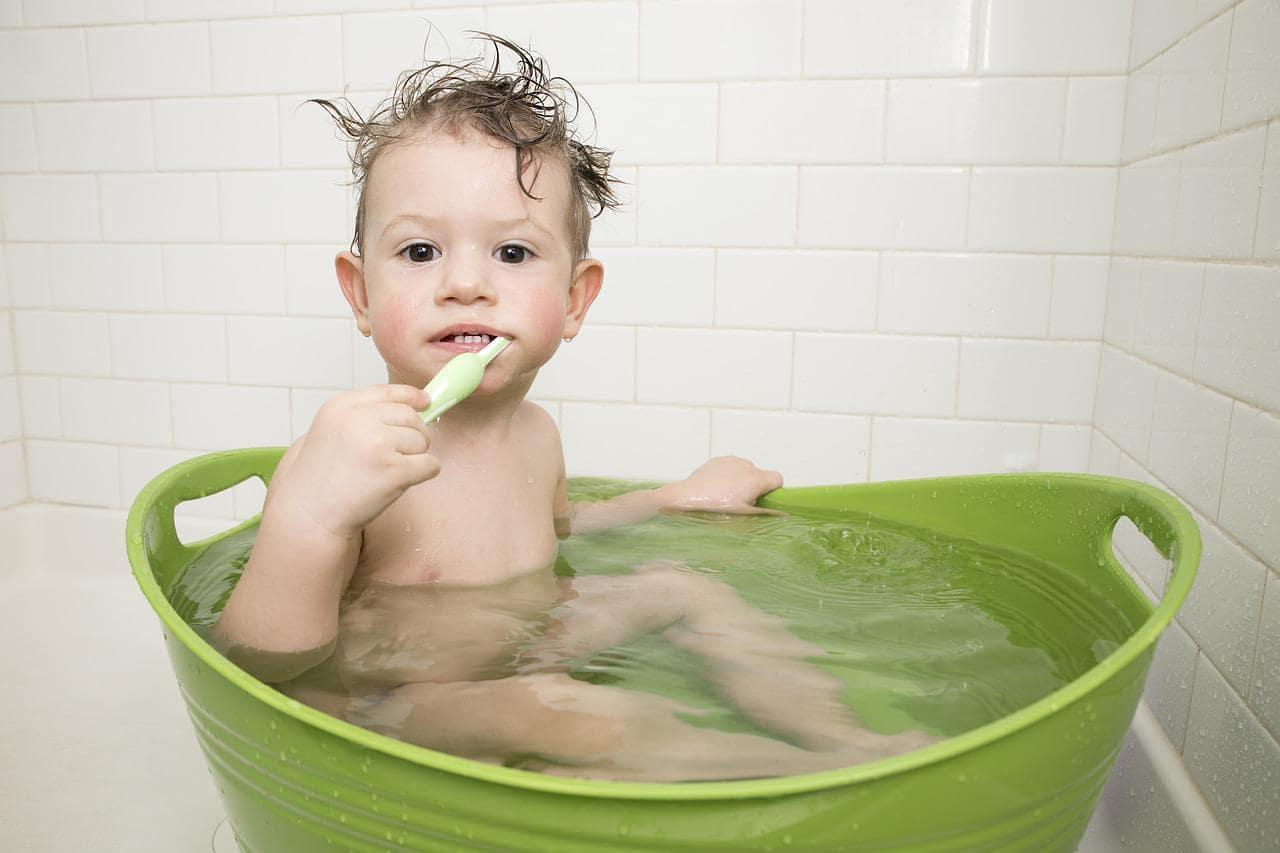A kid brushing teeth while in a tub with water 