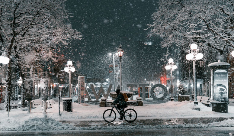 A person is commuting by bicycle through the snowy streets of Ottawa at night.