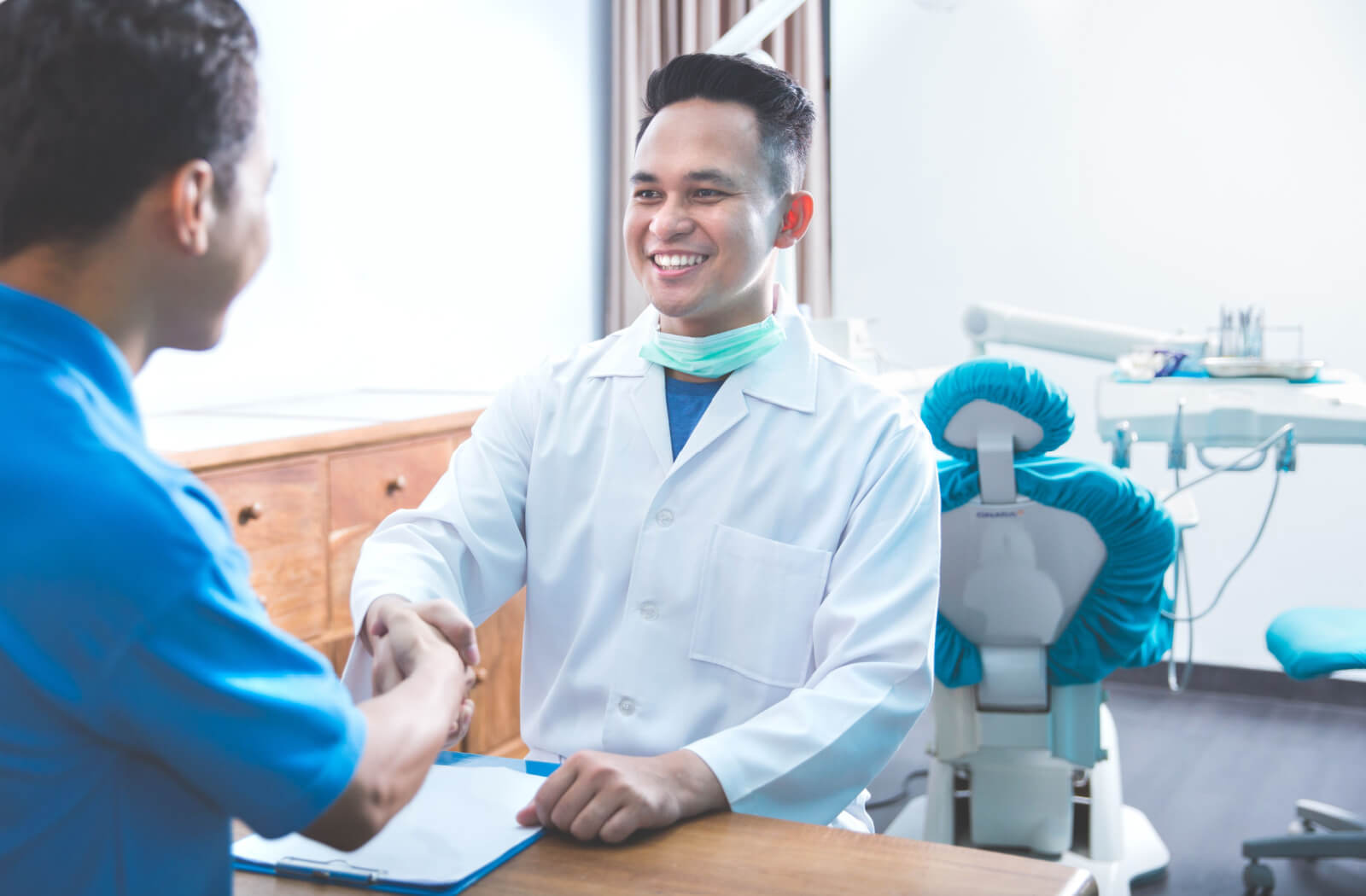 A man in a dental clinic shaking hands with his male dentist.