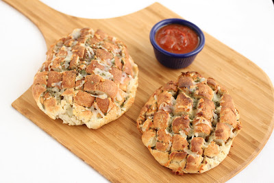 overhead photo of two Blooming Onion Pizza Breads on a board with a bowl of dipping sauce