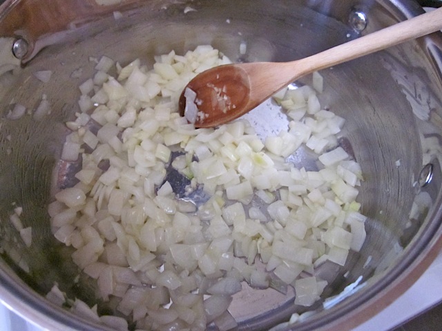 onion and garlic cooking in pot with wooden spoon 
