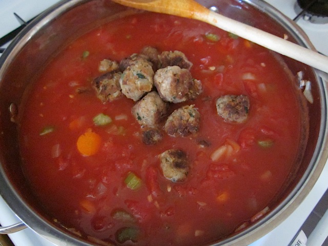 cooked meatballs being added to soup in pot 