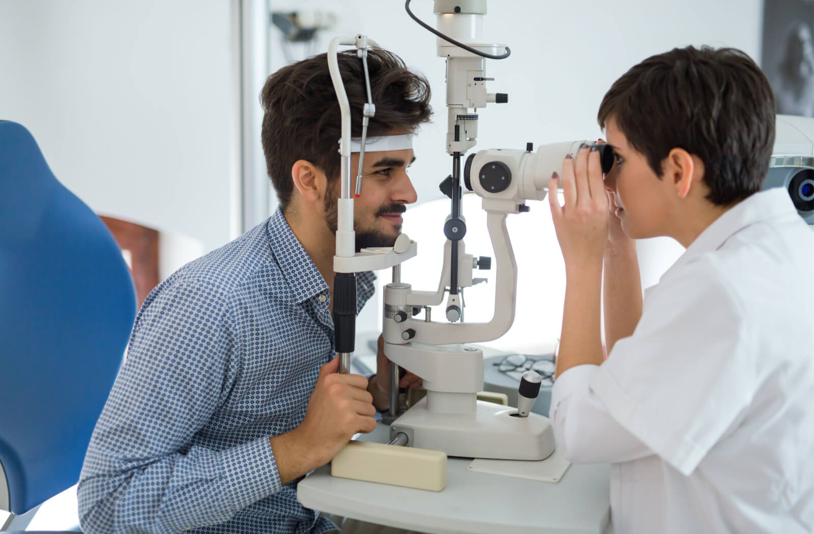A female optometrist using a medical device to examine the eyes of a male patient and look for potential eye problems.