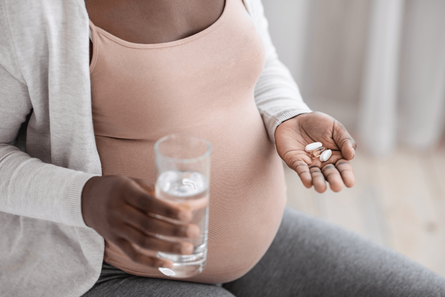 Pregnant woman holding prenatal vitamins and a glass of water