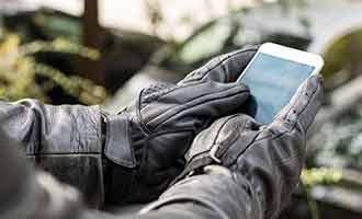 Focus is on an individual's hands as they wear leather gloves and text on their cell phone.