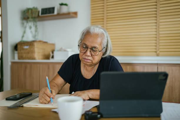 Senior woman home finance. Senior woman holding paper bills and calculating money expenses, using laptop for payments. cost of aging in place stock pictures, royalty-free photos & images
