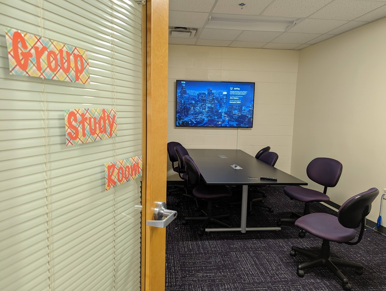 photo of group study room with large tv on the wall and 7 rolling office chairs around a table