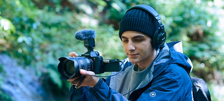 A cameraman is shooting in a natural environment, checking the sound with headphones. The camera is equipped with a ECM-B10 set to omnidirectional mode.