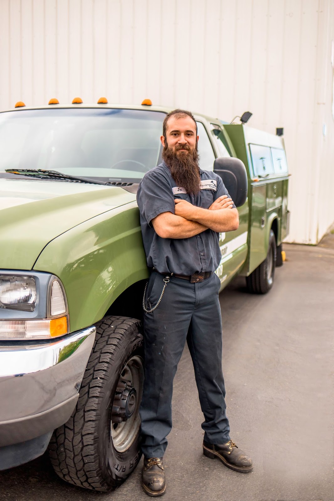 A close-up picture of a single mechanic leaning against a truck and smiling