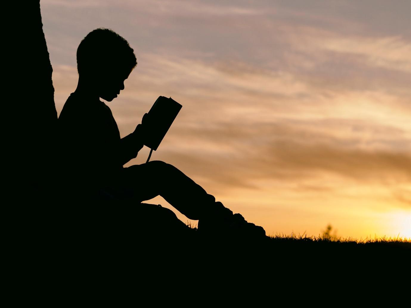 A silhouette of a child reading a bookDescription automatically generated